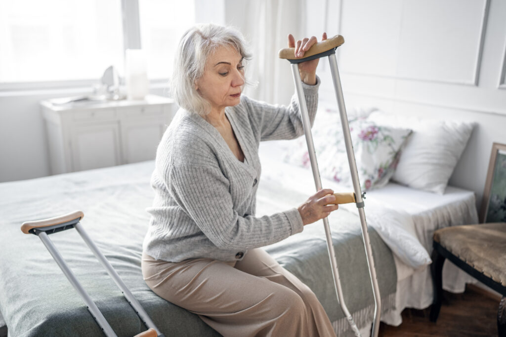 Elderly woman using crutches while standing up from bed during recovery after a fracture