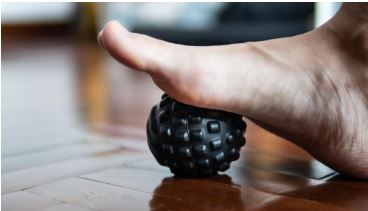 Foot rolling on a textured massage ball on the floor to massage the arch and relieve plantar fasciitis pain.
